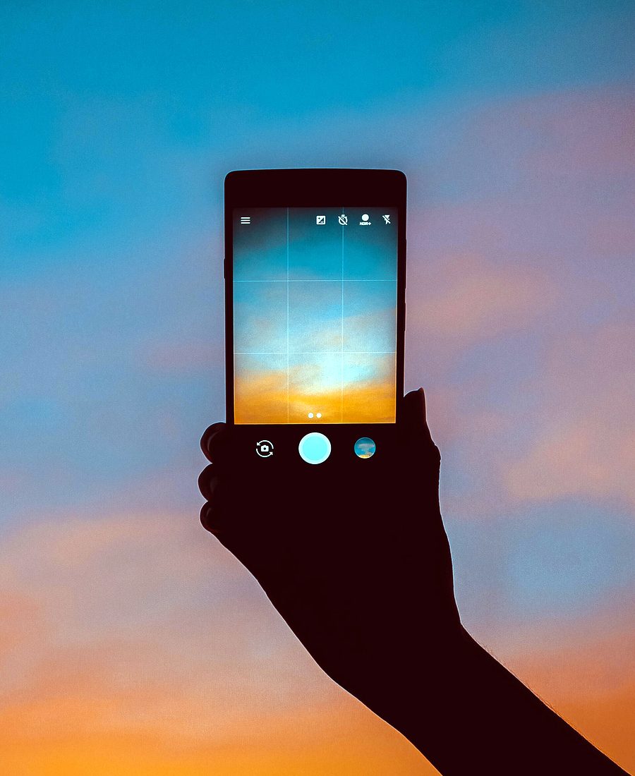 Smartphone tenu à bout de bras devant un ciel de crépuscule